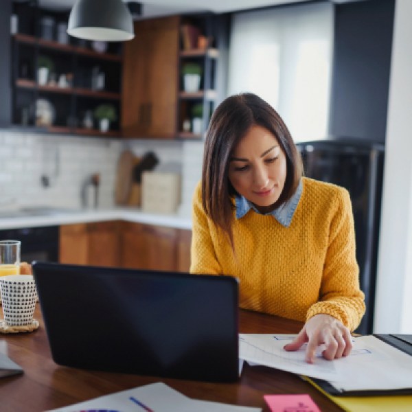 Woman in a bright yellow sweater working at laptop at a kitchen table